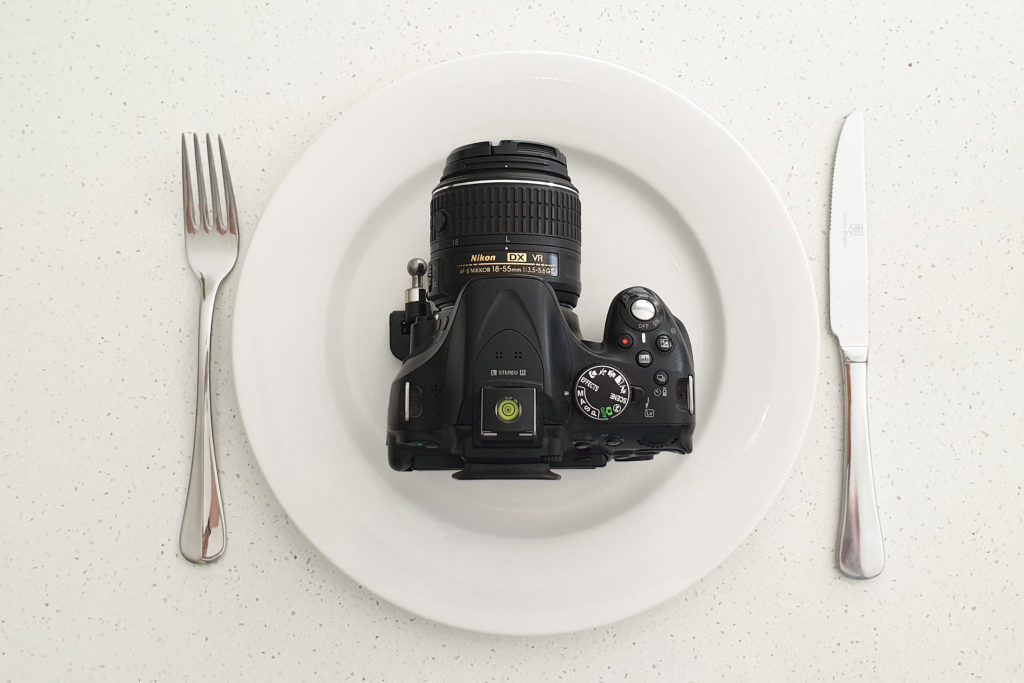best photography tips for beginners - a dslr camera on a white plate with a silver knife and fork next to it.