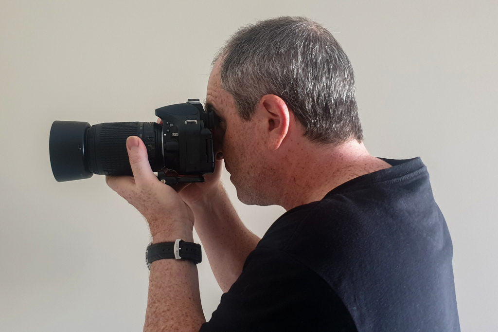 photography tips for beginners - a man holding a dslr camera viewed from his left side
