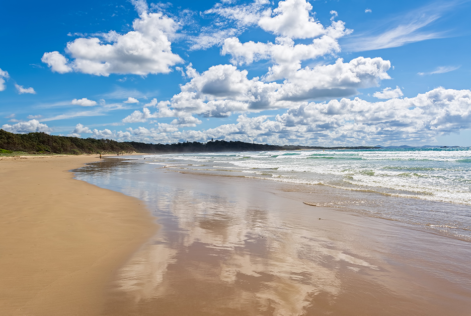 A beach on a sunny day with white clouds on a blue sky and waves rolling in