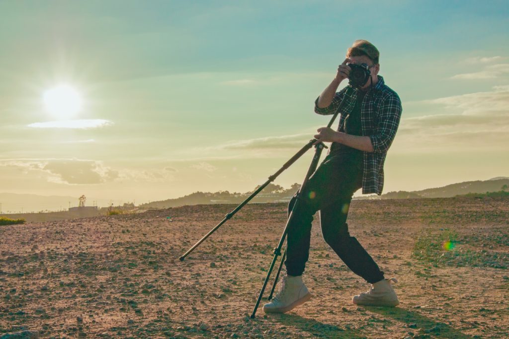 how to take sharp photos - man holding a camera on a tripod in the desert