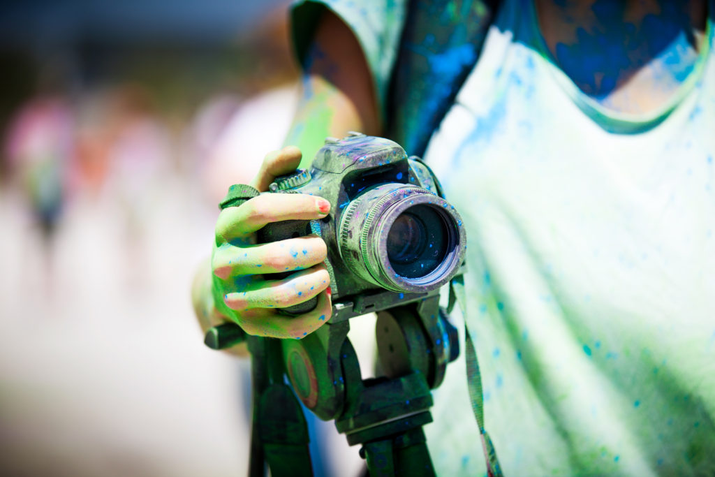 the importance of a clean camera lens - Woman hand holding a very dirty DSLR camera with green dust.