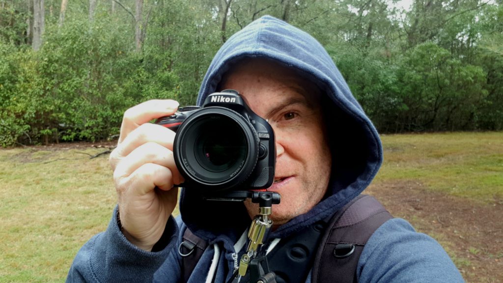 image of a man wearing a hoody, facing the camera, taking a photo