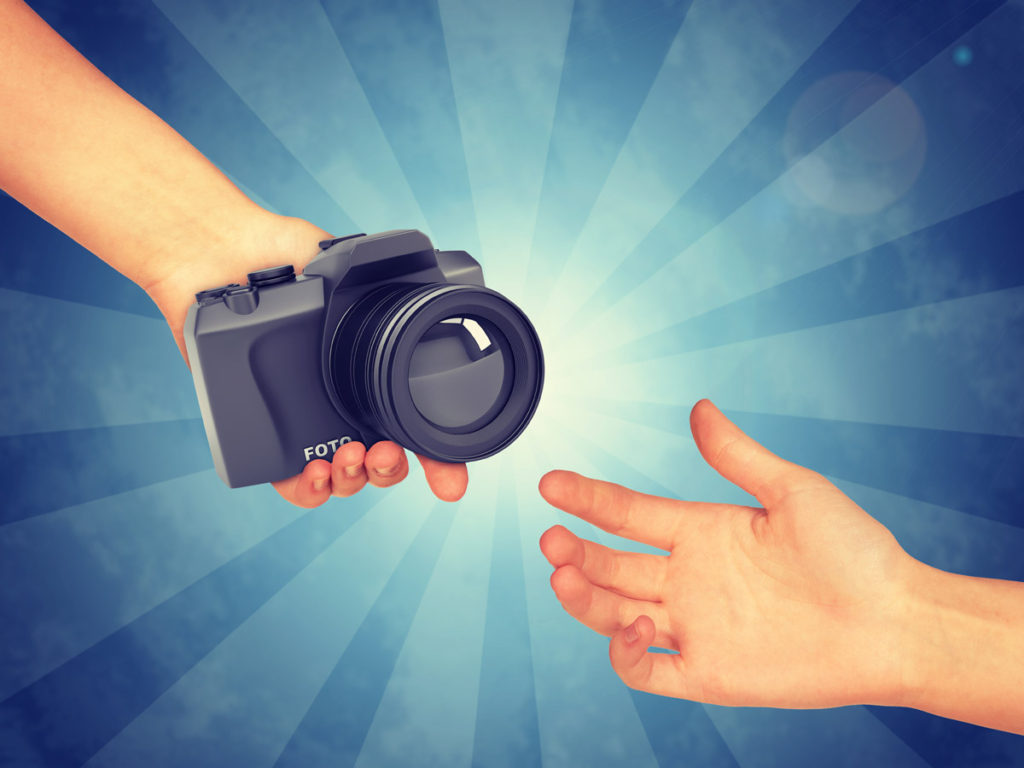 what is photograher's freedom - one hand passing a camera to another hand on a blue background with light rays