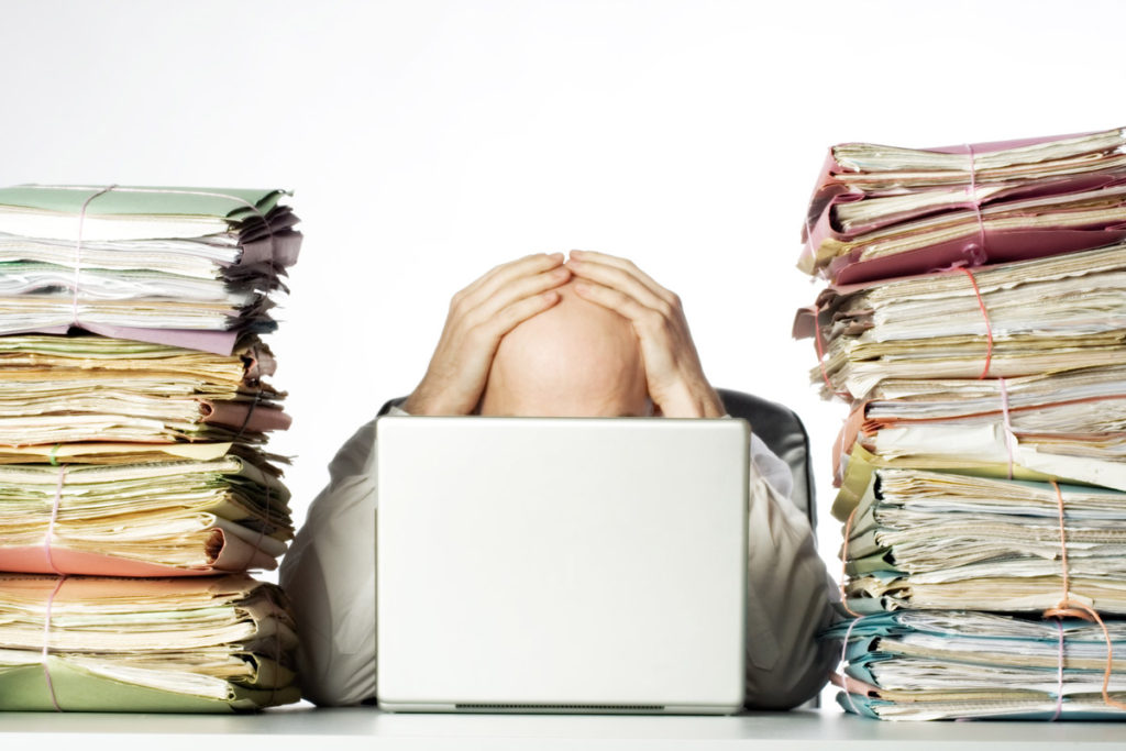 how to make more time for photography - man sitting behind a laptop between piles of paper 