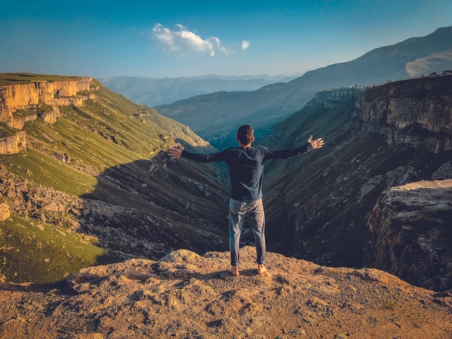 follow your passion - a man standing on a cliff with arms outstretched
