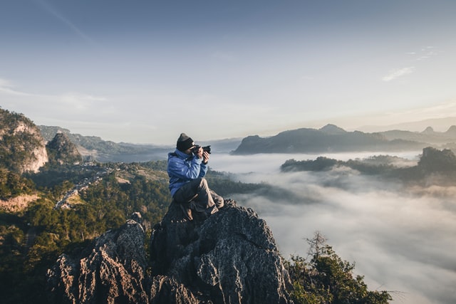 a photographer on a mountain top taking photos of a misty valley below