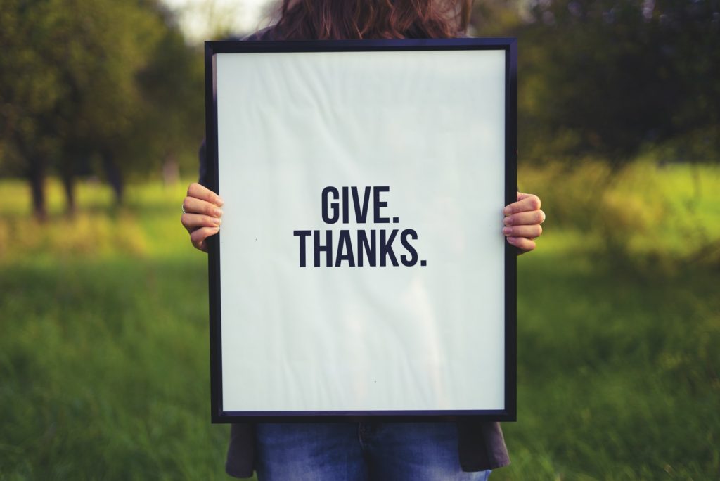 how to stop negative thoughts - woman holding up a frame with the words give thanks in it on white paper
