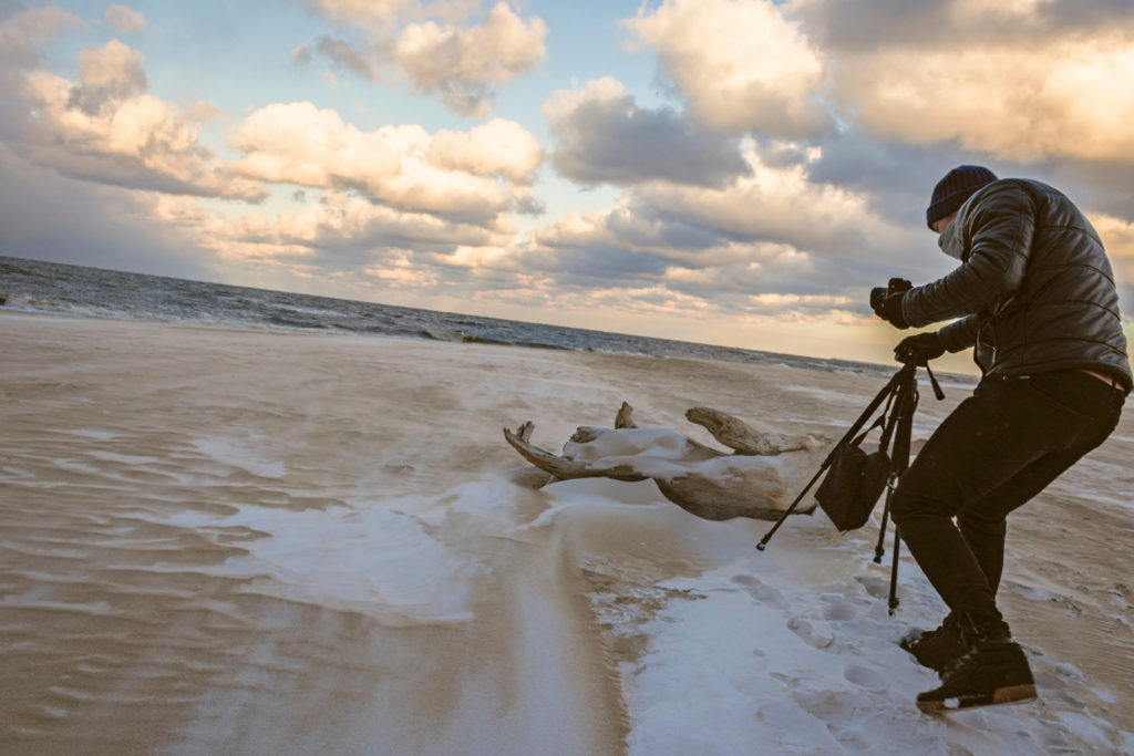 make money with photography as a beginner - man setting up a camera and tripod on snow